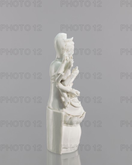 Guanyin on a lotus throne, Blanc de Chine porcelain, 18th century China Fujian, Chinese Buddhism iconography, goddess Guanyin, sculpture, height 27.0 cm, width 14.3 cm, A smooth white ceramic figurine stands against a flat light gray background, showing a seated figure with multiple layered arms and delicate hands arranged near its face and lap, a rounded head with subtle facial contours and a hood-like or headdress shape, flowing drapery forming a long garment that extends down into a cylindrical base with a banded detail, glossy highlights and soft shadows accentuating the sculpted folds and rounded forms, with visible seams and slight imperfections in the glaze.