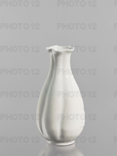 Vase, Chinese, Qing dynasty 1644–1911, decorated with peaches iconography, decorative vessel, dated 1690–1710, China; vessel; height 17.5 cm, diameter 8.4 cm., A glossy white ceramic vase with a fluted, wavy rim and a gently tapered, bulbous body standing on a rounded base, shown against a smooth gray background; the vase surface shows subtle crackle patterns and soft highlights and shadows, and the colors visible are white and shades of gray.