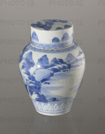 Storage Vessel with Lid, Zôshuntei Sanpo 1841–1878. Storage pot, blue-and-white porcelain, Arita, Japan, c. 1842–1878. Pear-shaped vessel with a flat cylindrical lid. Decorated in a Chinese-style landscape: an old man resting alone under a pine on a rocky cliff overlooking a wide body of water, contemplating a mountainous scene with waterfall, lofty peaks, and distant boat sails. Lower base features a wide ornamental band of three vertical and two crossed lines; neck and lower edge of lid have diagonal-line bands forming triangular motifs. Lid decorated with a rock motif. Decoration modeled on Chinese Southern School painting and the Japanese bunjinga nanga movement; free-form painting with precise, masterful lines. Cobalt in a bright, pure shade in several tones. Underglaze cobalt signature on the base: Zoshuntei Sampo zo made by Zoshuntei Sampo. Height 21.8 cm; diameter 15.3 cm., A porcelain jar with a lid featuring blue painted landscape motifs on a white background, showing brushst...