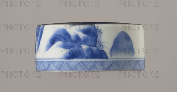 Storage vessel with lid by Zôshuntei Sanpo signed Zoshuntei Sampo zo, c. 1842–1878, Arita, Japan. Pear-shaped blue-and-white porcelain jar with flat cylindrical lid. Decorated in cobalt in several tones with a Chinese-style landscape: an old man resting under a pine on a rocky cliff overlooking water, with mountains, a waterfall, lofty peaks, and sailing boats on the horizon; lower base features a wide ornamental band of three vertical and two crossed lines; neck and lower edge of lid have diagonal-line bands forming triangles; lid decorated with a rock motif. Decoration modeled on Southern School Chinese painting and the Japanese bunjinga/nanga movement; free-form painting with precise, masterful lines. Height 21.8 cm; diameter 15.3 cm. Materials: blue-and-white porcelain. Periods: Edo–Meiji Edo 1603–1868; Meiji 1868–1912., An off-white cylindrical ceramic object with blue painted decoration around its side, featuring a stylized landscape motif with a group of rounded blue shaded form...