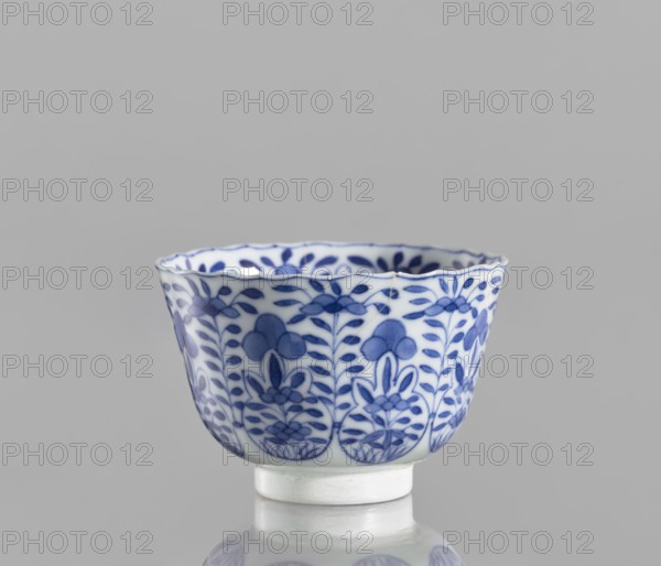 Bowl, Chinese, blue and white porcelain, ceramics, floral and plant ornaments, conical with a serrated rim, Kangxi period 1662–1722, Qing dynasty 1644–1911, 1662–1722, China, vessel; height 5.6 cm, diameter 7.9 cm., A small ceramic cup with a scalloped rim sits on a short foot, decorated all around with a repeating floral and leaf pattern in shades of blue on a white ground; the interior also shows blue leaf motifs; the background is a smooth light gray and the surface beneath the cup creates a soft reflection.