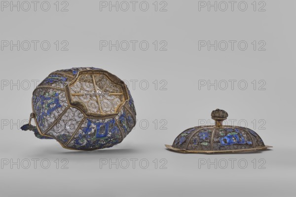 Basket with a lid; maker, Chinese; Canton, China; 19th century; material: not specified; subject: flowers, ornaments; function: container; dimensions: height 9.8 cm, width 10.5 cm, depth 7.5 cm., A pair of decorative metal objects sit against a light gray background, one tilted showing its underside and the other resting upright with a small knob on top; both have intricate openwork filigree with swirling patterns and are outlined with gold-colored metal, featuring several blue and green enamel floral and geometric inlays, and some darker metallic accents.