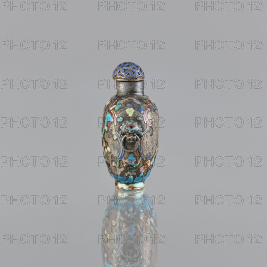 Snuffbox with stopper, cloisonné enamel, Chinese, figural scenes and plant ornament, handles, dated 1929–1930, vessel; height 5.8 cm, width 4.8 cm., A small ornate vessel with a rounded body and a narrow neck topped by a domed lid sits centered against a plain light gray background and casts a faint reflection on the surface below; the vessel displays a mix of colors including blue, turquoise, green, purple, gold, brown, and silver, with intricate raised decorative motifs and a sculpted ring handle on the front, and the lid features a lattice-like pattern in blue and gold.