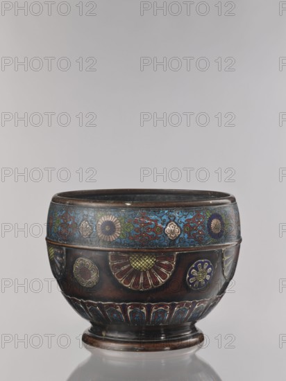 Flowerpot, Shimasa; creator/workshop, Japanese; Meiji period 1868–1912, late 19th century; champlevé enamel on bronze; floral ornament; jardinière vessel; height 30.4 cm, diameter 41.2 cm; provenance unknown, A rounded decorative bowl sits on a short pedestal base, showing a banded design and ornate floral motifs. The upper rim area features a patterned band with floral medallions and scrolling elements in shades of blue, green, red, and gold. The main body displays several floral roundels and a large stylized flower with petal-like segments in red, gold, and green against a dark brown ground. The lower portion has a repeating arch-like decorative band in blue and red with gold highlights. Visible colors include brown, blue, red, green, and gold.
