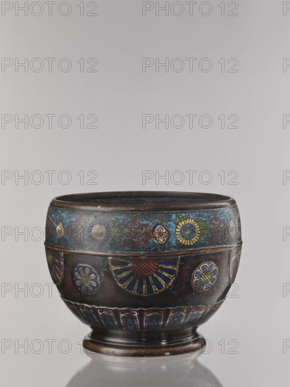 Flowerpot, Shimasa role/classification of creator, workshop author, Japanese, Meiji period 1868–1912, champlevé enamel, floral ornament, bronze jardinière, late 19th century, Japan; vessel; height 30.4 cm, diameter 41.2 cm; provenance unknown., A rounded decorative bowl with a short pedestal base sits against a neutral pale gray background; the bowl shows a dark brown metallic surface with bands of colorful enamel decoration featuring floral and geometric motifs in shades of blue, turquoise, green, yellow, red, and gold; a band near the rim displays a pattern of stylized flowers and scrolling shapes in blue and green with yellow accents, while the central section has larger circular floral medallions and fan-like designs in deep blue, red, yellow, and green; the lower rim bears repeating arch-like motifs in blue and red, and the interior appears dark, matching the bowl’s brown tone.