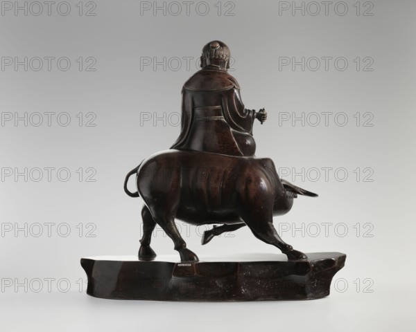 Laozi on a Buffalo, Chinese; Qing dynasty 1644–1911, 19th century; sculpture, figurine depicting Laozi on a buffalo; materials not specified; dimensions: height 39.5 cm, width 41.0 cm, depth 16.5 cm; subject: animals—buffaloes; cultural attribution: Chinese; date for Laozi ca. 550–500 BCE., A dark brown wooden sculpture of a person seated on the back of a bull, shown from behind on a low rounded rectangular base; the person wears a flowing robe with carved folds and has short hair with a rounded top, one arm bent holding a small object and the other resting by their side, while the bull has a curved tail, muscular haunches, and a lowered head with short horns, all rendered in smooth polished wood with visible grain and subtle surface variations against a neutral gray background with lighter tones near the bottom.