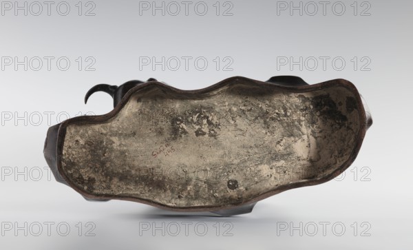 Laozi on a Buffalo;, ; Chinese; Qing dynasty 1644–1911; 19th century; sculpture, figurine; materials not specified; subject: Laozi ca. 550–500 BCE riding a buffalo; dimensions: height 39.5 cm, width 41.0 cm, depth 16.5 cm., A worn, shallow dish or tray viewed from above showing its interior surface with irregular, scalloped edges; the interior has a mottled, textured appearance with areas of lighter beige and darker brown-gray patches and scratches, while the rim and outer edge show a darker brown color; parts of a dark brown curved handle or spout are visible at the top edge; the background is a smooth gradient of light gray to off-white.