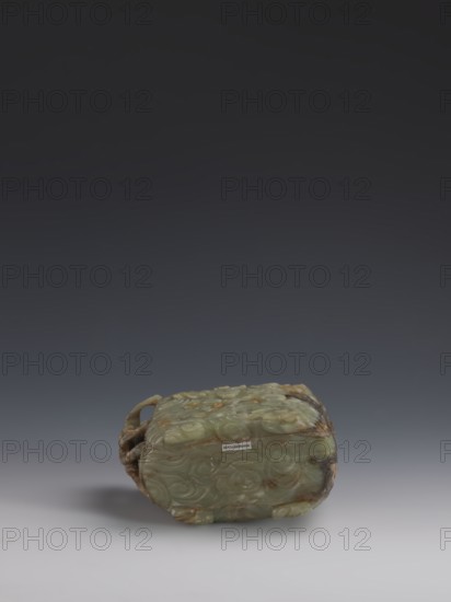 Vessel., Chinese, Qing dynasty 1644–1911, early 18th century. Gray-green jade, hollowed. Tall vessel on four feet with rounded edges; dragon-shaped handle on the narrower side. Entire surface covered in bas-relief motifs of clouds and mythological creatures dragons, clouds. Height 9.0 cm; width 14.0 cm; depth 6.5 cm., A carved object rests on a smooth surface against a dark gray to black gradient background, the object appearing predominantly pale green with areas of brown and darker green mottling; it has a rounded rectangular form with carved swirling patterns across its visible faces and a sculpted handle or loop at one side, and it casts a soft shadow on the surface beneath.