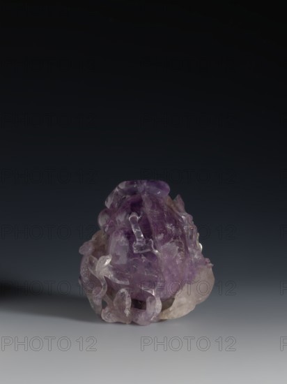 Pomegranate-shaped vessel, Chinese, Qing dynasty 1644–1911, decorated with pomegranates and frogs, 18th–19th century, China; vessel; height 10.2 cm, width 9.6 cm, diameter 7.2 cm., A translucent carved stone object with a dominant purple hue and areas of lighter, almost clear coloration sits against a smooth gradient background transitioning from dark at the top to lighter gray near the bottom; the stone has an irregular, rounded form with flowing carved details, smooth polished surfaces, and jagged inner textures, and casts a soft shadow to one side.