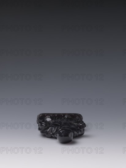 Buddhist monk, Chinese, monks, Qing style, Chinese art, Chinese Buddhism, Qing 1644–1911, Luohan iconography, 19th century, China, sculpture figurine; height 11.8 cm, width 7.1 cm, depth 2.0 cm, A small dark glossy sculpted object sits near the bottom center of the image on a smooth surface, showing a deep black color with highlights and subtle reflections; the object has rounded bulbous forms and flowing carved details suggesting organic shapes, with a slightly irregular silhouette and a polished finish; the background transitions from a lighter gray near the surface to a darker gray toward the top, creating a gradient of gray tones.
