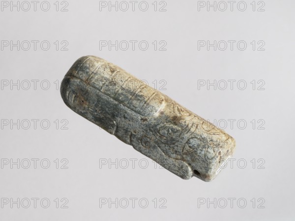 Tiger — tomb figurine; maker, Chinese; Western Zhou dynasty 11th century–771 BC; subject: tiger animal, zodiac; material: sculpture/figurine; function: tomb figurine; dimensions: height 2.6 cm, width 13.8 cm, depth 4.9 cm; weight 0.34 kg., A weathered cylindrical stone object with rounded ends floats against a plain light gray background, showing carved linear and curving grooves across its surface and a small notch at one end; the stone displays a mix of gray, beige, and greenish tones with darker gray and brown spots and worn lighter highlights.