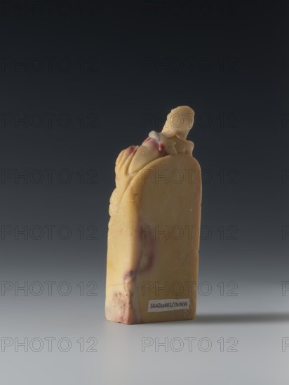 Seal stamp, purchase provenance noted; Chinese art; Chinese culture; Qing dynasty 1644–1911, Qing style; seal stamp depicting sages and officials; 18th–19th century, China; sculpture; height 8.2 cm, width 3.3 cm, depth 1.6 cm., A small carved object stands upright on a smooth surface against a dark gray to black gradient background; the object is primarily a warm yellow-beige with areas of reddish-brown marbling and faint white surface marks, and it has a sculpted rounded top with a small figure or rounded form integrated into the upper portion, showing smoother and slightly shinier contours where it is carved.