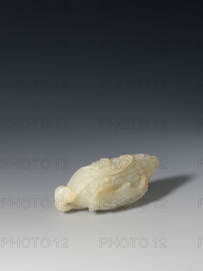 Paperweight - grapevine, Chinese, Qing 1644–1911, writing instrument, fruit grapes, pale green jade, 17th–19th century, China, sculpture; height 4.0 cm, width 10.3 cm, depth 4.8 cm, A small carved object with a smooth, slightly translucent surface in pale off-white and cream tones rests on a flat surface, showing areas of warm beige and faint yellowing; the carving features rounded, overlapping scale-like textures and flowing, curled forms with subtle glossy highlights and soft shadows, and casts a diffuse gray shadow toward one side against a gradient background that transitions from light gray at the bottom to dark charcoal at the top.