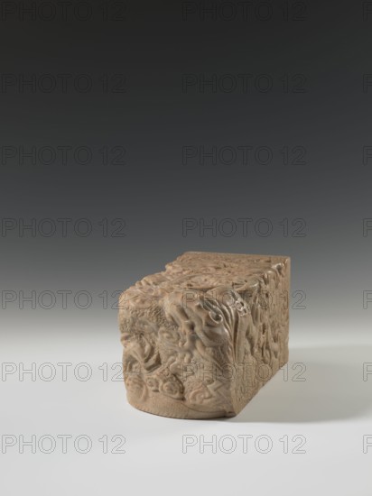 Seal stamp, Krieg doctor — Chinese seal stamp depicting a dragon with a pearl amid clouds; Qing dynasty 1644–1911, 18th–19th century; sculpture; materials not specified; dimensions: height 26.5 cm, width 12.2 cm, depth 12.5 cm; Chinese; iconography: dragons., A carved stone block with intricate raised reliefs sits on a smooth surface against a gradient background; the block shows swirling, organic motifs and rounded forms on its visible faces, with textured, curving lines and layered patterns suggesting flowing shapes. The object appears in shades of beige and light brown with subtle variations, cast shadows on the surface show tones of gray and soft white, and the background shifts from dark gray at the top to lighter gray near the horizon.