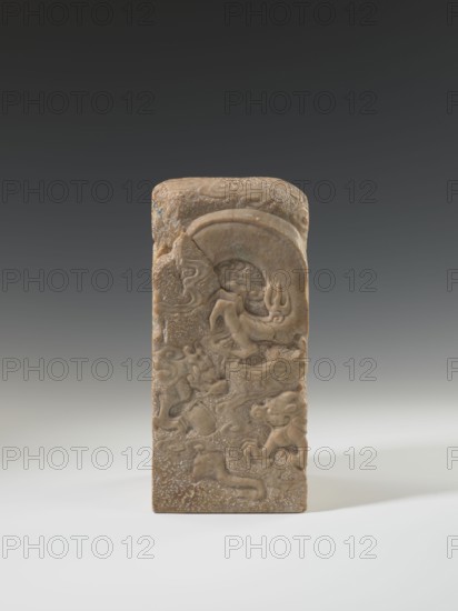 Seal stamp, Chinese art, Chinese culture, Qing dynasty 1644–1911, Qing style, seal stamp, dragon iconography, dragon with a pearl, 18th–19th century, China, sculpture; height 26.5 cm, width 12.0 cm, A rectangular carved stone object stands upright against a neutral gradient background, showing a brownish-beige color with lighter and darker variations; the front surface features shallow relief carvings of sinuous, flowing forms that resemble stylized creatures and cloud-like shapes, with curved arcs and rounded raised areas, and the top is slightly rounded with similar carved motifs and a textured, pitted surface.