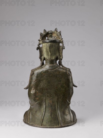 Guanyin;, Chinese; 17th century; China; Chinese Buddhism; bodhisattva; protective deities iconography; sculpture, figurine; height 43.0 cm, width 23.0 cm; purchase provenance., A back view of a seated sculptural figure made of dark greenish bronze with patches of brown and verdigris, showing a smooth rounded base and a flowing robe with vertical folds; the figure has a textured neck and hair visible as fine vertical grooves, and wears an ornate crown or headdress with curved and pointed elements and side ornaments that hang beside the head; the background is a uniform light gray.