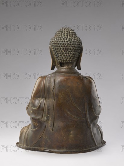 Shakyamuni Buddha, 17th/18th century China, Qing dynasty 1644–1911, Chinese Buddhism; sculpture height 47.0 cm, width 26.0 cm; tutelary deities and Buddha iconography, ushnisha; Chinese art, Qing style., A bronze statue shown from the back depicting a seated figure with a textured hair surface composed of small rounded bumps, elongated ears, and draped robes. The surface colors include dark brown, greenish patina, and hints of lighter brown highlights. The robe displays carved folds and a sash draped over one shoulder with subtle decorative patterns. The base is round and slightly flared, matching the bronze tones of the figure. The background is a smooth gradient of gray.
