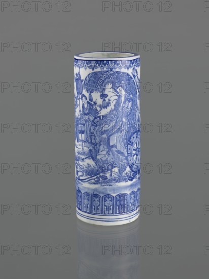 Vessel, Narozno Eckersdorf; Japanese ceramics, 19th century, Japan; figurative scenes with female images; decorative vessel; height 39.3 cm, diameter 15.5 cm; restitution provenance, A tall cylindrical porcelain vase with blue-and-white decoration stands against a gray background. The vase displays intricate blue painted scenes and patterns on a white ground, including stylized floral and geometric borders near the top and bottom and a detailed figurative scene around the middle showing a group of people in flowing garments and ornate headpieces, ornamental wheels, and foliage. The dominant colors visible are blue and white, with the surrounding backdrop in shades of gray.