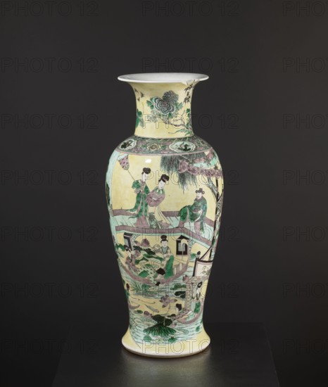 Vase, park scenes with architecture, enamel paints, Chinese art, Chinese culture, ceramics, decorative vessel, signed, 19th century, China, vessel, height 59.5 cm, diameter 25 cm, A tall ceramic vase with a flared rim sits against a dark background; the vase has a pale yellow base color with painted scenes in green, pink, purple, brown, and black, including a group of human figures wearing traditional clothing depicted around the body, architectural elements like railings and a small pavilion, stylized plants and lotus leaves at the lower section, decorative floral motifs near the neck, and delicate linework outlining faces and garments.