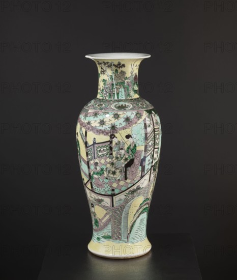 Vase, park scenes with architecture, enamel paints, Chinese art, Chinese culture, ceramics, decorative vessel, signed, 19th century, China, vessel, height 59.5 cm, diameter 25 cm, A tall porcelain vase with a flared rim stands against a dark background, decorated with intricate painted scenes and patterns in pastel greens, pale yellows, soft pinks, muted purples, black, and white. The neck shows stylized foliage and architectural motifs in green and yellow tones, while the bulbous body features a covered pavilion scene with several figures wearing flowing robes in green and pink hues seated on patterned flooring, surrounded by ornate drapery and carved railings. Decorative bands with floral and geometric designs encircle the shoulder, and the lower section displays arched architectural elements and landscape touches with water and plants rendered in green and pale blue. The base has a pale yellow ground and the overall surface is outlined and detailed in black against the soft colored ...