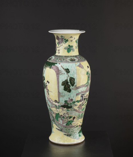 Vase by, enamel-painted park scenes with architecture, Chinese ceramics decorative vessel, signed, 19th century, China; height 59.5 cm, diameter 25 cm., A tall ceramic vase with a flared rim sits against a dark background, showing a pale yellow base color with painted scenes in green, pale turquoise, pink, brown, and black; the neck displays floral and leaf motifs in green and pink, the shoulder has a decorative band with green and pink details, and the body features a painted narrative scene with figures in traditional dress in green and pink, architectural elements in pale turquoise and brown, leafy trees in dark green, and water and lotus motifs in pale turquoise and green.