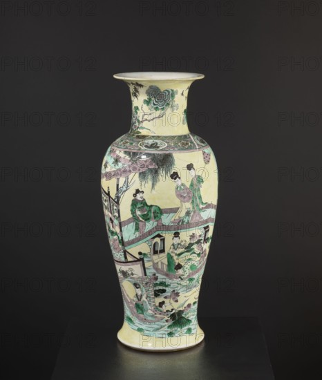Vase, park scenes with architecture, enamel paints, Chinese art, Chinese culture, ceramics, decorative vessel, colored porcelain, 19th century, China, vessel, height 59.5 cm, diameter 25.5 cm, A tall ceramic vase with a flared rim against a dark background, predominantly pale yellow with decorative scenes painted in green, pink, black, and teal; the upper neck shows floral motifs in green and black, a band of ornate geometric and floral patterns encircles the shoulder, and the body features a continuous narrative scene with a group of figures wearing robes, architectural elements like railings and bridges, a boat, flowing water, and stylized plants and lotus leaves in green and pink tones, with additional black linework and shaded areas for detail.