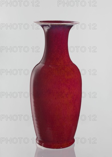 Vase, Chinese, Qing dynasty 1644–1911, ceramics decorative vessel with sang de boeuf bull's blood glaze. Large oval vase with a long wide neck opening at the spout. 19th century, China. Height 58 cm; diameter 24.5 cm., A tall glossy vase with a flared rim and a narrow neck widening into a rounded body, shown against a plain light background; the vase is primarily deep red with variations of darker and slightly lighter red tones and subtle speckled texture, and there are highlights reflecting off its shiny surface that appear white.