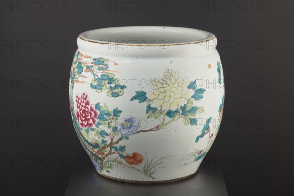 Pool — aquarium., Chinese, Qing dynasty 1644–1911, 19th century. Colored porcelain vessel decorated with chrysanthemums, lotuses, and images of birds; bulging form narrowed at the bottom. Height 41.5 cm; diameter 41.1 cm., A rounded ceramic vessel with a glossy pale off-white surface decorated with painted floral and branch motifs in colors including teal, blue, green, pale yellow, pink, red, orange, and brown, showing a large pale yellow blossom, a deep pink blossom, a blue blossom, leafy branches with teal and green leaves, and small orange and red fruit-like shapes, with a slightly weathered brown rim and a narrow brown base, set against a dark gray background.