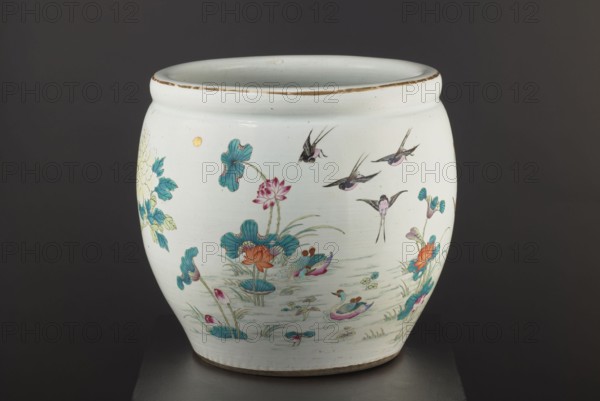 Pool - aquarium, Chinese art, Chinese culture, Qing 1644–1911, Qing style, aquarium ceramic vessel decorated with chrysanthemums, lotuses, and images of birds, colored porcelain, pool-shaped decorative vessel, bulging, narrowed at the bottom, 19th century Qing dynasty, China, height 41.5 cm, diameter 41.1 cm, A rounded ceramic vessel with a white base color sits against a dark gray background, decorated with a painted scene of aquatic plants and birds; the decorations include teal and green leaves, turquoise and teal lily pads, orange and pink flowers, and small stylized ducks with pink, blue, and green feathers floating on pale blue water, while several small birds with black and pink markings are depicted flying above; there are also touches of gold and brown along the rim and in small round accents, and the vessel rests on a neutral-colored base.
