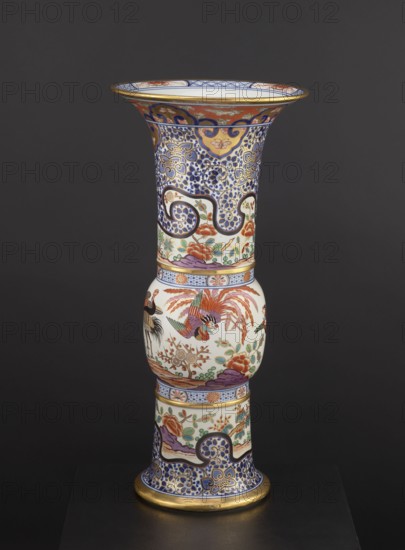 Vase, Japanese, ceramics, colored porcelain Imari, 19th century. Vessel with floral decorations, phoenixes iconography, lambrequin pattern; height 66.5 cm, diameter 31.3 cm., A tall decorative vase with a flared rim and pedestal base set against a dark gray background, featuring intricate painted patterns and figurative scenes; the top rim has a band of gold, the neck area displays dense blue and white scrolling floral motifs with accents of gold and orange, and a section with stylized cloud-like shapes in dark blue and gold. The central bulbous midsection is primarily white with colorful painted birds and floral arrangements in shades of red, orange, green, purple, and black, with additional small green foliage and brown branches. The lower pedestal echoes the blue and white scrolling pattern with gold highlights and includes panels of floral imagery in red, orange, green, and purple, while the base edge is gilded in gold. Overall visible colors include blue, white, gold, red, orange,...