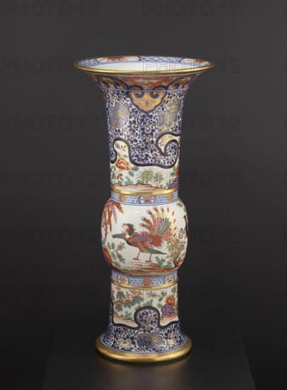 Vase, Japanese, 19th century, colored porcelain Imari, ceramics; floral decorations, phoenixes iconography, lambrequin pattern; decorative vessel; height 66.5 cm, diameter 31.3 cm., A tall decorative vase with a flared rim and a bulbous midsection stands against a dark background, showing a rich palette of blue, white, gold, red, green, and purple; the upper section features dense blue and gold scrolling floral patterns with a few ochre medallions and a white interior rim with blue and red accents, the midsection displays a white rounded panel with a colorful bird rendered in red, green, orange, and gold perched among stylized plants and foliage in green and red, and the lower section continues the ornate motif with blue and gold filigree, floral scenes in green, red, and purple, and gold bands at the base and rim.
