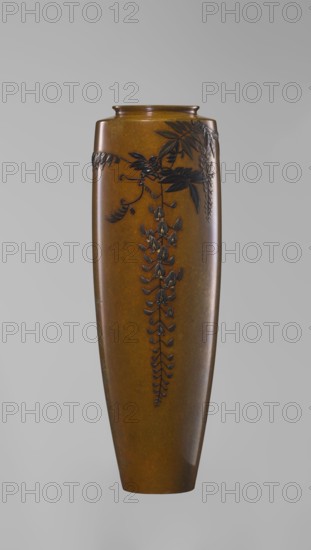 Vase, Nogawa role classification of creator, workshop; A slender miniature vase with a belly widening slightly toward the top and narrow, straight arms. There is no neck, and the spout is in the form of a flat ring. The bottom is round, slightly recessed, with an engraved brand. Decoration: a naturalistically treated wisteria vine placed in the upper part of the belly on one side, with a sumptuous flower cluster hanging down almost to the end of the vase. Made of silver with gilding and black shakudo patina, combining various metals and alloys to produce a darker tone for the decorative motif against the background, achieving colorfulness and naturalistic yet decorative effect. Meiji period, ca. 1890–1900. Japan, Kyoto. Vessel. Height 15.7 cm; width 5.3 cm., A tall, narrow vase with a smooth, glossy surface in shades of brown and amber, decorated with a raised, dark brown floral vine motif that trails down the front; the vine includes several elongated leaves and clusters of dangling f...