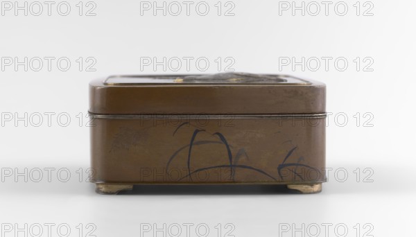Box with a lid, Jômi, Eisuke I 1839–1899 artist; rectangular box with rounded corners, decorated on the flat lid with two flying wild geese made in high relief with inlay of silver and gold iro-e zogan technique. The side walls are decorated with a motif of inclined reeds, made of silver and shakudo using the hira-zogan technique, producing a painted effect. The lid bears a gold signature in a square field with two stylized kanji characters resembling archaic forms: Shobi. Ca. 1880–1899 Meiji period, 1868–1912. Japan, Kyoto. Container. Height 4.8 cm; width 10.2 cm; depth 11.4 cm., A small rectangular metal box with rounded corners and a lid sits on a plain light surface against a pale background; the box is predominantly brown with darker brown edges and faint darker markings on its sides, featuring a few curved dark blue brushlike strokes and a subtle darker brown leaflike motif, and it rests on small worn metallic feet that show a golden-beige tone.