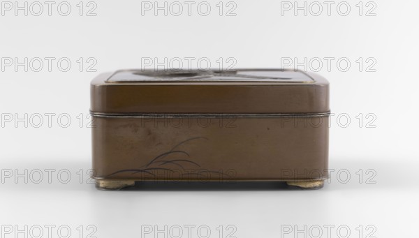 Box with a lid, Jômi, Eisuke I 1839-1899 artist; geese, grass; Rectangular box with rounded corners, decorated on the flat lid with two flying wild geese made in high relief with inlay of silver and gold iro-e zogan technique. The side walls are decorated with a motif of inclined reeds, made of silver and shakudo using the hira-zogan technique, i.e., the decorative motif is level with the background surface, giving a painted effect. On the lid there is a gold signature in a square field with two stylized kanji characters resembling archaic ones: Shobi. Ca. 1880–1899 Meiji Period, 1868–1912, Kyoto, Japan. Container. Height 4.8 cm; width 10.2 cm; depth 11.4 cm., A rectangular metal box with rounded corners sits on small curved feet, shown from the front against a pale background; the box is primarily brown with darker brown and black decorative lines suggesting a simple plant motif on the lower front panel, and there are thin metallic edges and a slightly darker band where the lid meets ...