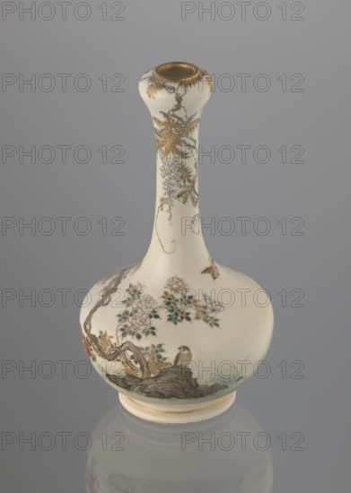 Vase, Yabu Meizan 1853–1934, c. 1900 Meiji 33, Osaka, Japan. Onion-shaped vase on a low ring foot with a long, slender neck bulging at the spout. Decorated in kachôga flowers-and-birds motif: a small delicately hatched black-and-gold ornament in the lower belly; a golden-leafed wisteria vine with white blooms entwining the neck, growing from the rock on which a sparrow perches; a tall rose bush with white and red blooms beside the wisteria; two sparrows painted in gold and iron black flying around the plants. Warm, milky glaze with very fine cracklework; thin gold stripe around the foot and gilded rim. Painter’s mark in gold at the bottom: in a square cartouche, three kanji characters: Yabu Meizan. Ceramic vessel, height 15.0 cm, diameter 8.0 cm., A slender-necked ceramic vase with a rounded body sits against a neutral gray background; the body of the vase is an off-white or cream color with delicate painted decoration featuring a group of flowers with green leaves, a small bird perche...