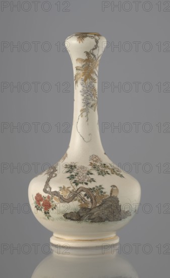 Vase, Yabu Meizan 1853–1934, c. 1900 Meiji 33, Japan, Osaka. Onion-shaped vase on a low ring foot with a long slender neck bulging at the spout. Decorated with a freely composed kachoga flowers-and-birds motif: a small delicately hatched black-and-gold ornament on the lower belly; a golden-leafed wisteria vine with white blooms entwining the neck, growing from a rock where a sparrow perches; a tall rose bush with white and red blooms beside the wisteria; two sparrows painted in gold and iron black flying among the plants. Warm, milky glaze with very fine crackle; thin gold stripe around the foot and gilded rim. Gold-painted maker’s mark at the bottom in a square cartouche with three kanji characters: Yabu Meizan. Ceramics; height 15.0 cm, diameter 8.0 cm., A pale cream ceramic vase with a long narrow neck and a rounded bulbous base sits against a gray background; the surface features painted botanical motifs including a twisted brown branch, clusters of green leaves, delicate pale blos...