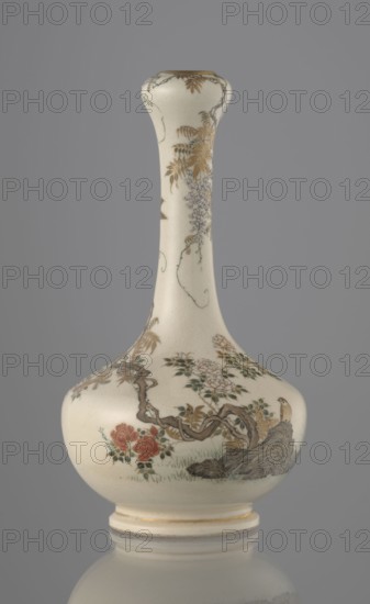 Vase, Yabu Meizan 1853–1934, c. 1900 Meiji 33, Osaka, Japan. Onion-shaped vase on a low ring foot with a long, slender neck bulging at the spout. Decorated with a freely composed kachoga flowers-and-birds motif: a small, delicately hatched black-and-gold ornament on the lower belly; a golden-leafed wisteria vine with white blooms entwining the neck and growing from the rock where a sparrow perches; a tall rose bush with white and red blooms beside the wisteria; two sparrows painted in gold and iron black flying around the plants. Warm, milky glaze with very fine cracklework; thin gold stripe around the foot and gilded rim. Gold-painted maker’s mark at the bottom in a square cartouche with three kanji characters: Yabu Meizan. Ceramic vessel; height 15.0 cm, diameter 8.0 cm., An off-white ceramic vase with a long narrow neck and bulbous base sits against a gray background; the vase is decorated with painted floral and botanical motifs in gold, brown, green, red, muted purple, and black, ...