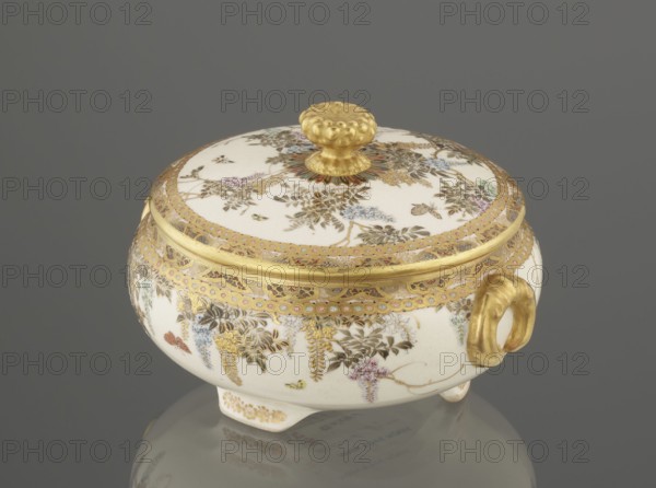 Small box with a lid, Kinkôzan, Sôbei VII 1867–1927 author, Kinkôzan workshop, Japanese art, Japanese culture, Meiji 1868–1912, wisteria, ceramics, butterflies, boxes, satsuma. The lid has a gold knob in the shape of a flower. The vessel has two slightly convex handles, on three wide feet. Signed, late 19th century Meiji period, Japan, Kyoto, Awata. Vessel, container; height 6.8 cm, diameter 10.2 cm., A small decorative round lidded bowl with a domed lid and a floral knob, resting on a reflective surface; the bowl is primarily white with extensive gold trim and accents, including a gold rim, a gold patterned band around the lid, and a gold handle; delicate painted floral and foliage motifs in green, blue, pink, purple, brown, and pale yellow decorate the white surface, with fine gold detailing interwoven among the flowers; the knob on the lid is textured and gold, and the bowl stands on small feet with gold embellishment; the background is a uniform gray.
