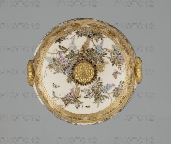 Small box with a lid, Kinkôzan, Sôbei VII 1867–1927 author, Kinkôzan workshop, Japanese, Meiji period late 19th century, Japan — Kyoto, Awata. Satsuma ceramics vessel/container decorated with wisteria and butterflies. The lid has a gold knob in the shape of a flower; the vessel has two slightly convex handles and stands on three wide feet. Signed. Height 6.8 cm; diameter 10.2 cm., A circular porcelain object seen from above with a white background area decorated with floral and insect motifs in colors including gold, green, pink, blue, brown, and black, a central raised gold rosette surrounded by a ring of petal-like shapes in dark green, red, and gold, an ornate gold patterned border encircling the rim, and two gold handles protruding from opposite sides.