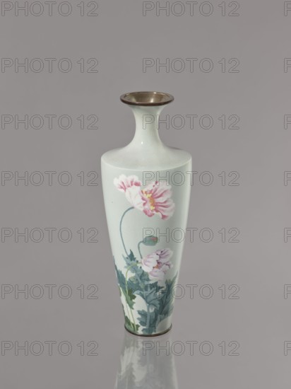 Vase, gift, cloisonné enamel, Symmetrical decoration: blooming poppies on a grey-blue background; flowers poppies. Meiji–Taisho period, ca. 1910–1920. Nagoya, Japan. Vessel; height 24.5 cm, diameter 9.0 cm., A tall, slender vase with a flared neck and rounded lip sits against a plain background. The vase is a pale, light greenish-white color with a glossy surface and a metallic rim at the top and base. Painted on its body are delicate floral motifs: a few large pink flowers with layered petals and pale yellow centers, accompanied by stems and a cluster of bluish-green leaves at the lower portion. The vase casts a soft reflection on the surface beneath it. The visible colors include pale greenish-white, pink, yellow, bluish-green, metallic bronze, and muted gray from the background and reflection.