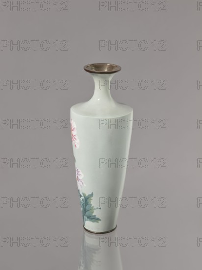 Vase, cloisonné enamel; symmetrical decoration of blooming poppies on a grey-blue background; flowers poppies; Meiji–Taisho period, ca. 1910–1920; Nagoya, Japan; vessel; height 24.5 cm, diameter 9.0 cm., A tall, slender vase with a narrow neck and flared rim, shown against a plain gray background; the vase is a pale celadon color with a metallic bronze-colored rim at the top and a matching metal band at the base, and it bears a painted floral design featuring soft pink blossoms and blue-green leaves on one side, with the vase reflected faintly below it.