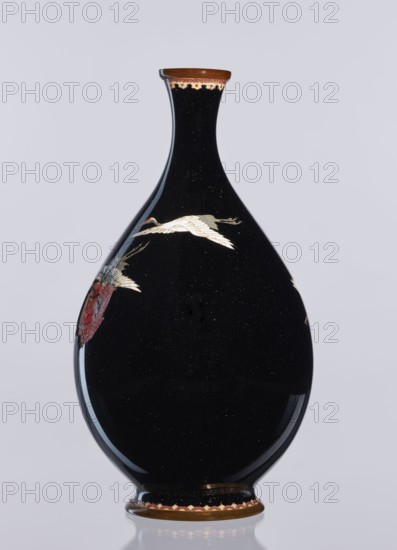 Vase, cloisonné enamel, Meiji period 1868–1912, Nagoya, Japan; 19th/20th century. Decorative vessel vase depicting birds—cranes; height 18.3 cm, diameter 10 cm., A glossy teardrop-shaped vase with a narrow neck and flared rim, predominantly black with a subtle speckled sheen, decorated with a few stylized white birds in flight and accents of red and gold; the rim and base have brown and gold edging with a scalloped red-and-cream patterned band, and there is a small area of muted red decoration on one side.