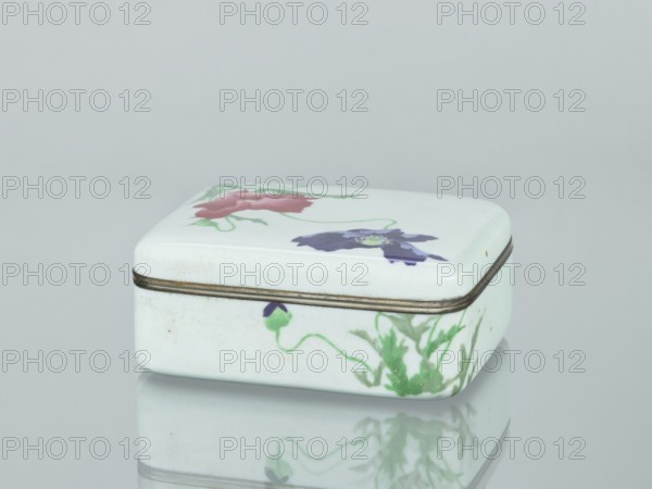 Box with a lid; maker, ; poppies; Japanese art; Japanese culture; flowers iconography; plant ornament; decorative cloisonné enamel vessel; Taisho period, ca. 1912–1926; Japan; box; height 4.7 cm, width 11.1 cm, depth 8.8 cm., A small rectangular ceramic box with rounded corners sits on a reflective surface; the box is predominantly white with painted floral motifs in red, purple, green, and a hint of yellow, and it has a thin metal band around the lid edge that appears slightly tarnished.