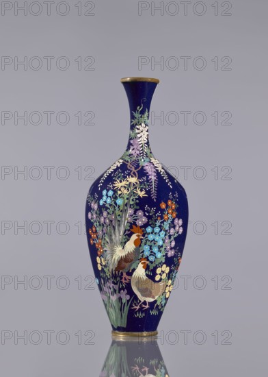 Vase, cloisonné enamel, wisteria, hens, flowers, roosters iconography, Japanese art, Meiji 1868–1912, ovoid vase elongated with a long thin neck slightly flared at the spout, navy blue background of the decoration, c. 1890–1910, Japan, vessel, height 15.6 cm, dia. 5.6 cm, width 6.4 cm, A tall vase with a narrow neck and rounded body sits against a plain light gray background, its surface a deep navy blue adorned with a detailed floral and bird design in colors including purple, lavender, light blue, turquoise, orange, yellow, green, brown, white, and gold; the painted scene shows a pair of birds with brown and white feathers among clusters of various flowers and long green leaves, with cascading floral elements near the neck and a gold rim at the top and base, and a reflection of the vase visible on the glossy surface beneath.
