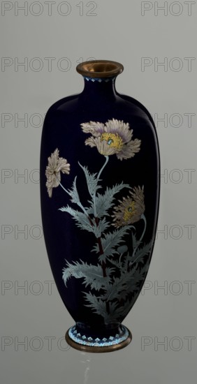 Angular vase one of a pair with rounded edges, on a low round foot and with a short neck slightly flaring at the spout. The bottom of the foot and the edge of the spout are framed in silver-plated copper. Against a uniform dark garnet background with a purple hue, a decoratively but faithfully depicted tall flower grows from the base of the vessel to the neck. Stems with alternating, elongated, jagged leaves in pale grayish green support large, full corollas of white and light purple flowers with dense yellow stamens and a green pistil; the motif is executed using the yusen cloisonné enamel technique, with thin silver wires precisely structuring the delicate, jagged forms of leaves and petals. Plant stems are accentuated with chocolate brown enamel. The flowers are rendered slightly differently on each vase of the pair, enhancing naturalness. Around the foot and neck is a border of small geometric semicircle and rhombus motifs in white and two shades of blue, also in the yusen techniqu...
