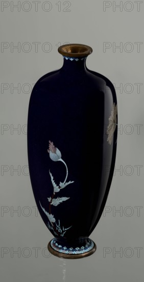 Vase, flowers, poppies, Japanese art, Meiji 1868–1912, cloisonné enamel, vases, Japanese culture. Angular vase one of a pair with rounded edges, on a low round foot and with a short neck slightly flaring at the spout. The bottom of the foot and the edge of the spout are framed in silver-plated copper. Against a uniform dark garnet background with a purple hue, a decoratively but faithfully depicted tall flower grows from the base and reaches the neck. Stems with alternating, elongated, jagged leaves in pale grayish green support large, full corollas of white and light purple flowers with dense yellow stamens and a green pistil; the motif is executed using the yusen technique, with thin silver wires precisely structuring the delicate, jagged forms of the leaves and petals. The plant stems are accentuated with chocolate brown enamel. The flowers are presented slightly differently in each vase, enhancing naturalness. Around the foot and neck there is a border of small geometric semicircle...