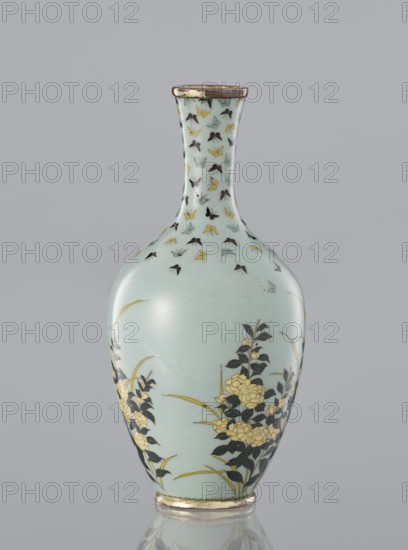 Vase with a thin, very slightly flared neck decorated with flowers and butterflies in cloisonné enamel on a pale blue-gray background. Japanese, Meiji/Taisho period, ca. 1910–1920. Height 11 cm; diameter 5.3 cm., A smooth, slender vase with a narrow neck and rounded body sits against a plain background; its surface is a pale bluish-green with decorative motifs in black, yellow, and a muted blue-green, including a group of small stylized winged shapes near the neck and floral clusters with dark leaves and yellow blossoms toward the body, plus thin curved stems in yellow; the rim and base have metallic bands with a slightly worn appearance.