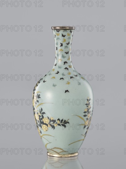 Vase, Cloisonné enamel with flowers and butterflies on a pale blue-gray background. Meiji–Taisho period, ca. 1910–1920. Japan. Vessel with a thin, very slightly flared neck. Height 11 cm; diameter 5.3 cm., A pale blue-green porcelain vase with a narrow neck and rounded body sits against a neutral gray background, decorated with a scattered pattern of small butterfly-like shapes in black, yellow, and light blue across the neck and upper body, and floral branches with dark leaves and pale yellow blossoms on the lower sides, with thin gold-colored curved accents near the base and a metallic rim at the top.