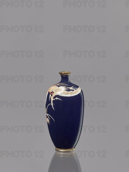 Vase, Japanese, Meiji period 1868–1912, cloisonné enamel, 19th–20th century. Subject: Japanese dragon motif/icons of dragons. Vessel; height 36.7 cm, diameter 4.6 cm. Repossession Kraków; ., A single narrow vase stands against a plain gray background; the vase is deep navy blue with a glossy finish and has a small rounded neck and flared rim finished in gold. A decorative motif wraps around the upper portion of the vase featuring a stylized bird with pale cream and gold feathers and a small area of red near its head, along with flowing cream-colored lines suggesting long tail feathers. The base of the vase has a gold band, and the vase casts a soft reflection on the smooth surface beneath it.