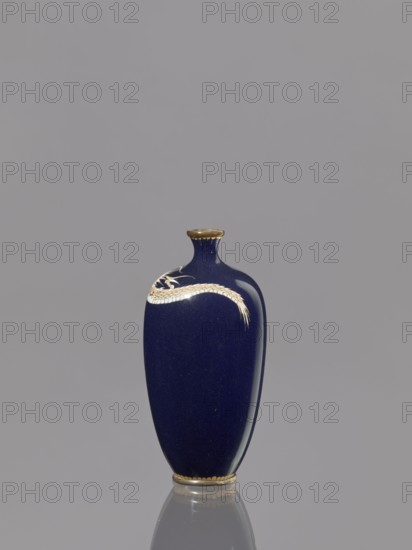 Vase, Meiji 1868–1912, cloisonné enamel, Japan, 19th/20th century; subject: Japanese dragons dragon motif/iconography; vessel; height 36.7 cm, diameter 4.6 cm., A tall vase with a deep blue glossy surface stands against a plain gray background, showing a smooth curved form with a narrow neck and small flared rim that is edged in a gold color; a gold-colored decorative motif resembling a sinuous band or stylized dragon wraps near the upper portion of the vase, and the base also has a gold-colored band; the vase casts a faint reflection on the surface below, and the visible colors are deep blue, gold, and gray.